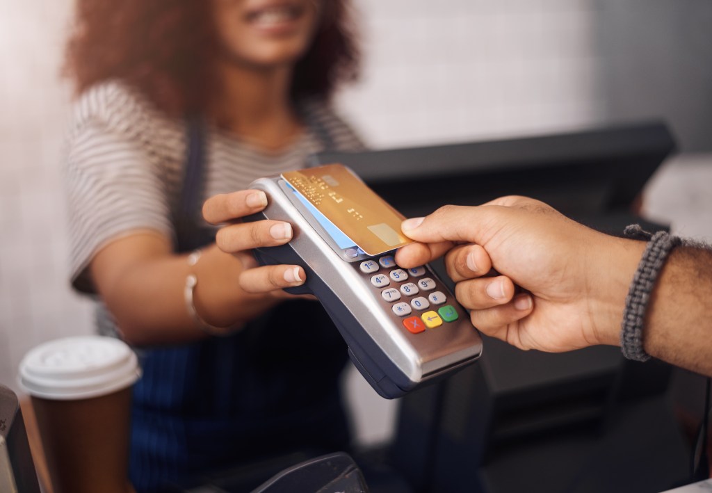 Customer making a contactless payment with a credit card at a coffee checkout using an NFC-enabled point-of-sale machine